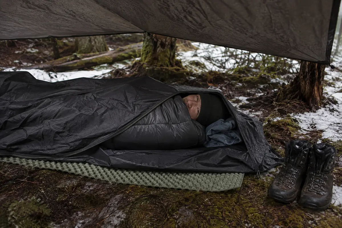 Eingepackte Person in Schlafsack und Biwaksack unter einem Tarp