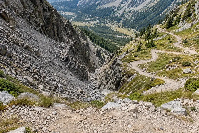 Ein Serpentinenweg führt rechts neben einer steilen felsigen Schuttrinne ins tiefere Tal