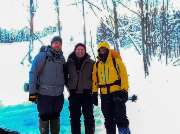 Drei Personen in Winterkleidung stehen in verschneiter Landschaft