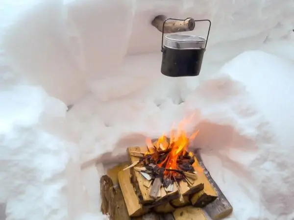 Ein Kochtopf hängt über einem Feuer auf einem Holzstapel im Schnee