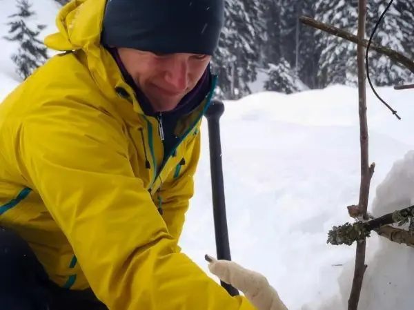 Ein Mann in gelber Jacke baut eine Konstruktion aus Ästen im Schnee