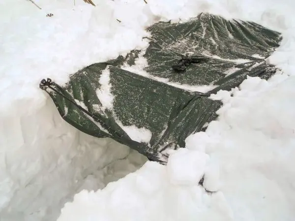Grüne Plane liegt im Schnee neben einer Schneeverbarrikade