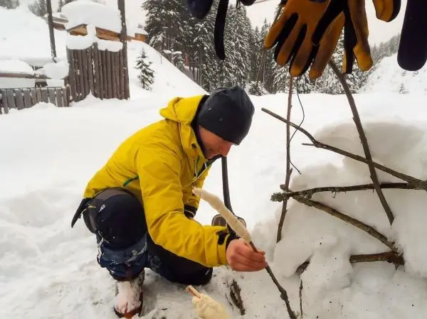Person baut eine Struktur aus Ästen im Schnee beim Überlebenstraining