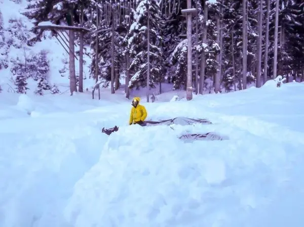 Person in gelber Jacke gräbt im Schnee neben einem Zelt