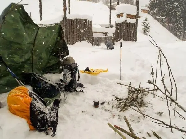 Zelt steht im Schnee, Rucksäcke und Äste liegen herum