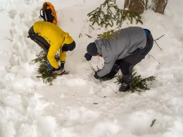 Zwei Personen binden Äste im Schnee zusammen beim Überlebenstraining