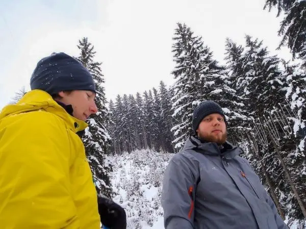 Zwei Personen stehen im Schnee zwischen hohen, verschneiten Bäumen