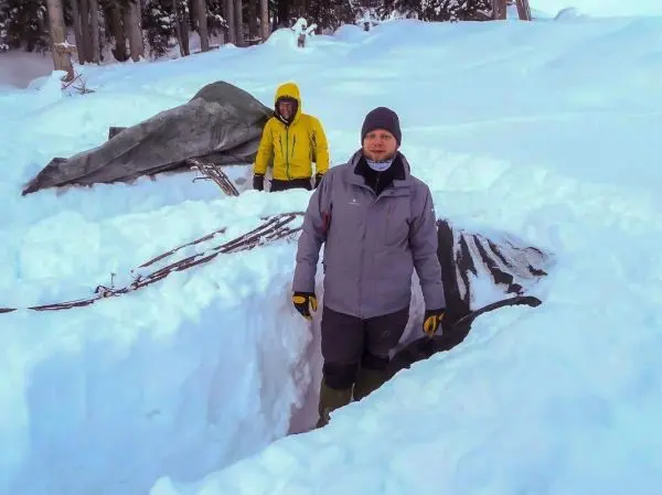 Zwei Personen stehen in einer Schneelandschaft neben einer Tarp-Notunterkunft